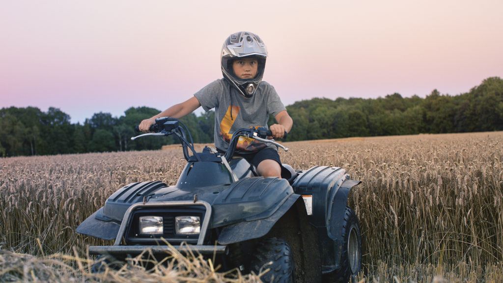 Pojke på fyrhjuling på ett sädesfält