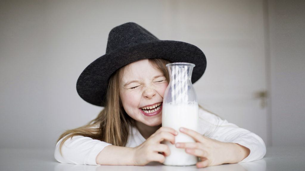 Flicka med hatt skrattar och håller i en flaska mjölk